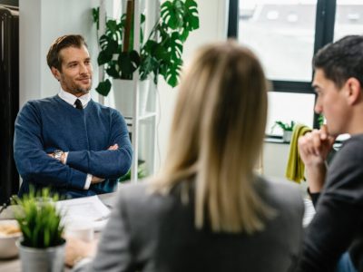 Smiling financial advisor sitting with arms crossed and talking to a couple about their future investment plans.